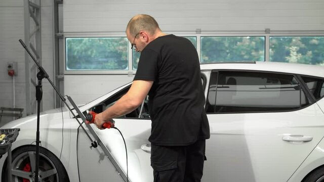 Man Professional Car Mechanic Is Heats The Door With Hot Air Gun And Fix Dent Without Painting Using Tools. Process Of Repairing Dent On Door By PDR Method.