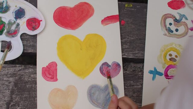 Children paint hearts with paints during the open air. Love sign. Painting workshop for kids. Art enhances the development of motor skills. 