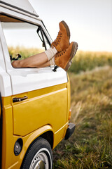 legs peeping out of van's window. alternative way of travel and enjoy the world. discover new places and live with nature view. cropped young caucasian female have rest in classic van, relax - obrazy, fototapety, plakaty