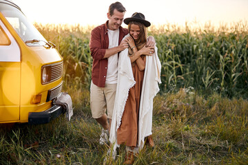 It's getting cold. young happy Hippie couple on trip in countryside. yellow retro style van vehicle...