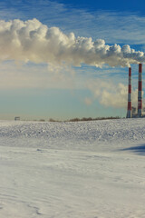 Winter landscape, snow-covered field and in the distance there are CHP chimneys on the horizon and...