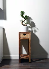 Schilderijen op glas Ginseng ficus bonsai plant in white pot on table with  drawer and shadow on wall © Brett