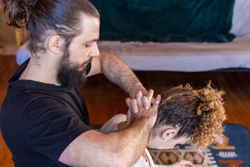 Naklejka premium A professional masseur, is seen from the side with clasped hands applying pressure to the head and neck of female client with copy space in top right.