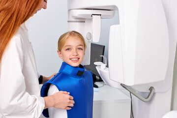 caucasian child girl patient doing panoramic teeth x-ray orthopantomography in dental clinic in protective clothes, Side view. medical healthcare concept. beautiful kid with dental doctor