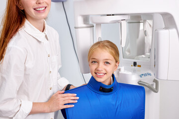 Caucasian Redhead Female dental specialist is going to examine an x-ray of smiling child in modern dental clinic by professional specialist. little caucasian kid has dentist checkup. Portrait