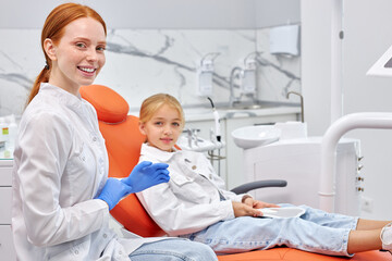 Obraz premium Cute nice Female dentist is wearing gloves before curing teeth cavity. Dentist caries treatment for child girl at dental clinic office. People, medicine, stomatology and health care concept