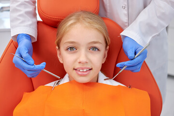 Happy caucasian Child girl came to see the dentist. Kid sits in dental chair. Professional dentist bent over her, top view. Happy patient and dentist concept. Adorable child look at camers smiling