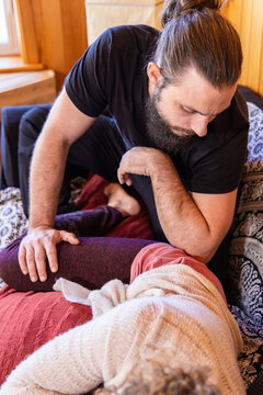 A caucasian man with beard and hair tied back in bun, performs a Shiatsu massage technique on a relaxed woman seen in soft focus in foreground.