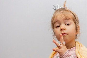 A little girl in a crown looks at the rings on her fingers, children's jewelry and bijouterie.