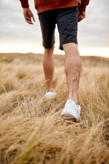 Cropped male in sneakers standing on fluffy grass in the field,unrecognizable guy is engaged in sport, cale to walk or run. sport, fitness, people, active healthy lifestyle concept