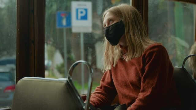 Cinematic shot of young woman in face mask during corona virus regulations, travel in tram or bus. Woman in public transport during 2022 corona rules. Travel regulation limitations
