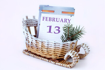 Calendar for February 13: decorative sleigh with a loose-leaf calendar inside, name of the month in English, number 13, fir branch, white background