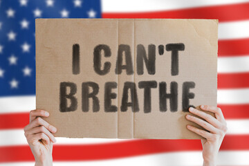 The phrase " I can't breathe " on a banner in men's hand with blurred American flag on the background. Discrimination based on skin color. Murdered by police. Officers violent rights. Brutality. Death