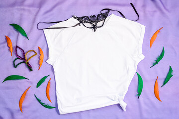 Mockup white t-shirt decorated carnival mask and colorful feathers. Mardy Gras apparel flatlay on...