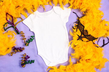 Mockup white baby bodysuit decorated yellow feather boa and carnival mask. First Mardy Gras baby...