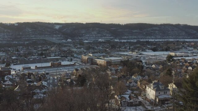 A slow forward winter aerial establishing shot of a Pennsylvanian small town at sunset. High school building in the foreground. Pittsburgh suburbs. Summer version available.  	