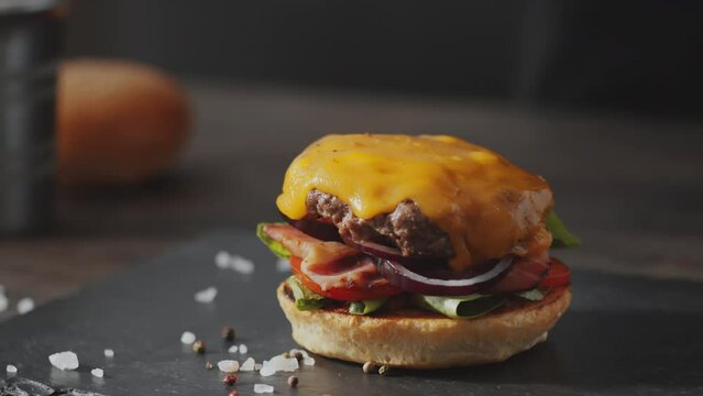 Close up selective focus shot of hand of chef adding sauce to delicious burger and then putting half of bun on top