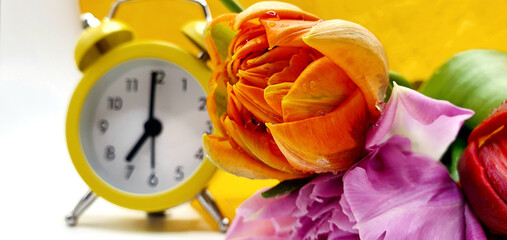 Yellow alarm clock and flowers tulips on the table. Spring time and spring flowers. Beautiful tulips. Good morning. Have a good day. Fresh flowers background.
