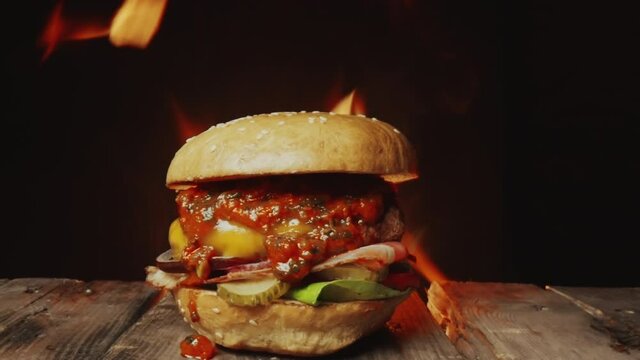 Zoom in shot of delicious homemade burger on wooden table with burning fire in background