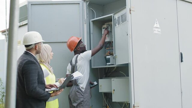 Electrician in safety helmet checking voltage levels of solar panels in switchgear. Equipment Power Distribution Cabinet. Electrician Engineer Tester Measuring Voltage Current Power Electric Line