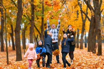 Portrait of a family with children in an autumn city park - happy people walking together, they toss the leaves, beautiful nature with yellow leaves as background.