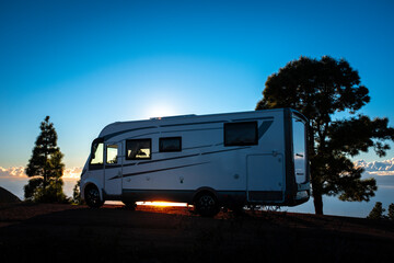 Camper van parked against sunset light and trees. Concept of alternative lifestyle vanlife and travel wanderlust. Summer holiday vacation with camping car recreational vehicle