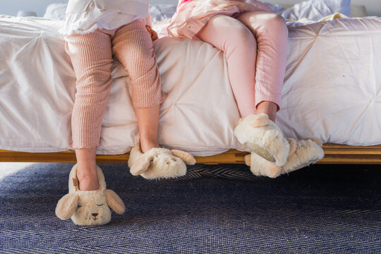 Little Kids Wearing Cute Slippers Sitting On Bed