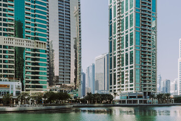 Fototapeta na wymiar Modern city skyscrapers buildings at sunset time with business and residential towers around the lake and palm trees