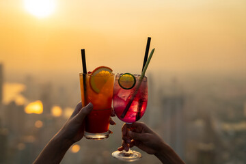 Beautiful Asian woman friends meeting and drinking cocktail together at skyscraper rooftop restaurant in metropolis at summer sunset. Female friend enjoy outdoor lifestyle activity in the city at nigh