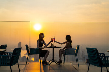 Beautiful Asian woman friends meeting and dinner party together at skyscraper rooftop restaurant in...