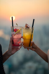 Beautiful Asian woman friends meeting and drinking cocktail together at skyscraper rooftop...