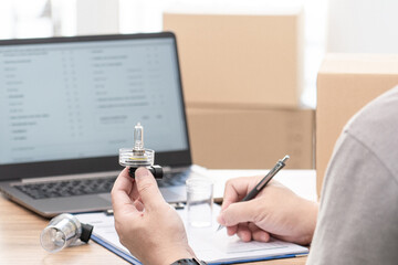 Close up hand a man hold car headlight bulb halogen and bulb case, check detail of part for car service concept and use laptop and checklist in service office store in car service center