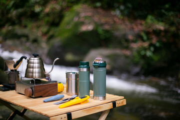 Thermo bottle on wooden camping table in in camping area. selective focus