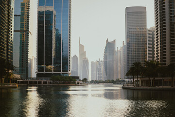 Fototapeta premium Modern city skyscrapers buildings at sunset time with business and residential towers around the lake and palm trees