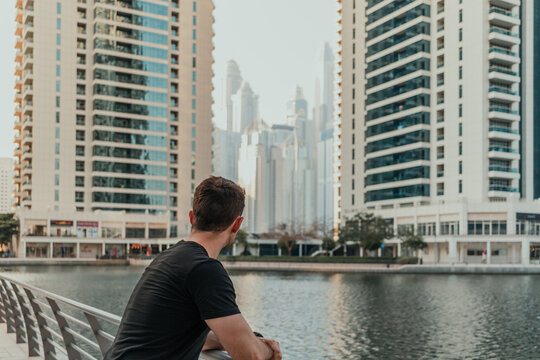 Young person standing outdoor and looking forward to the urban background with city skyline and skyscrapers around the lake