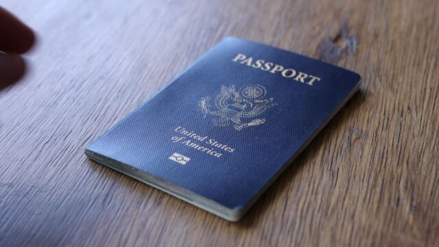 One human hand placing a blue American passport on a wooden desk
