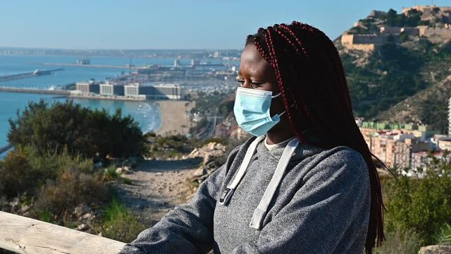 Black woman taking off face mask sitting against sea background