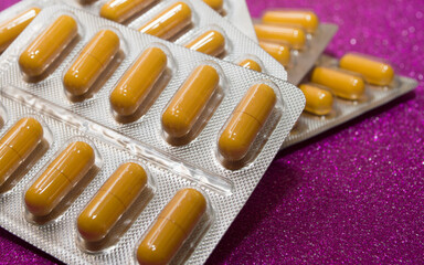 yellow capsules pills pills in a silver blister on a crimson background close-up