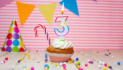 Happy birthday card for the age of three on a pink background. Beautiful number 3 happy birthday background, with burning multi-colored candles in a muffin and a candy cane. Festive background with co