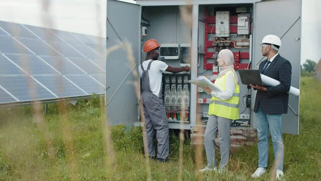 Electrical Systems Equipment Power Distribution Cabinet. Multiracial people examining process of green energy production. Power transformer. Multiracial people checking switchgear on solar station.