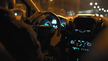 Man driving car through the streets of night city. View from the back seat of the car.