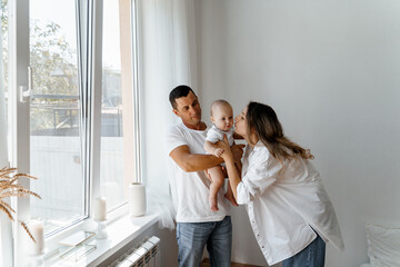 mom and dad are standing at the window with a baby, a young family