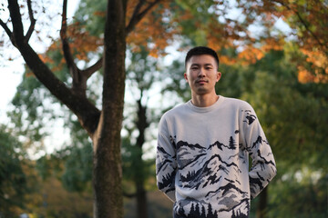 One Asian young man in sweater at natural park under tree in autumn