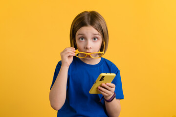 Little Girl 9s in Basic Blue T-shirt and Yellow Glasses Using Smartphone Scrolling and Reading...