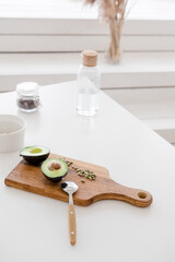 A still life sliced avocado with pumpkin seeds lies on a wooden board on a white table, against the background of a bottle of water