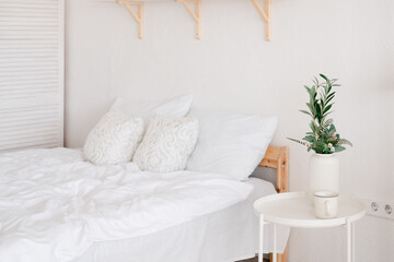 White cozy bedroom with a green plant on the table. Empty bed with a white bedding set,