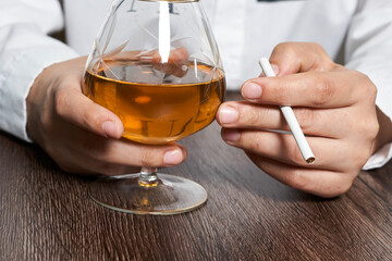 Person holding alcohol glass and cigarette in the bar, concept of drinking alcohol and smoking