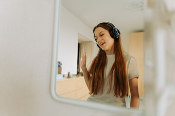 Beautiful girl of generation Z in headphones, singing at the mirror at home