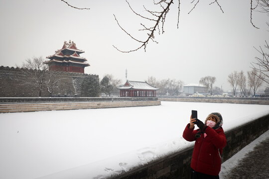 A woman takes pictures of the Forbidden City after an overnight snowfall as the spread of COVID-19 continues, in Beijing