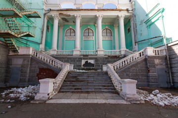 rear entrance of the house of culture requiring restoration. turquoise theater building with stairs and columns. fire escapes from the back of a city building